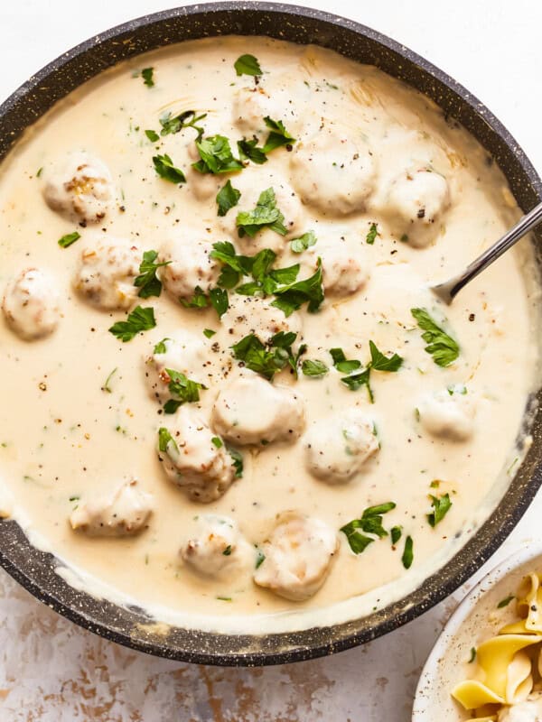 A bowl of pasta with meatballs and parsley.