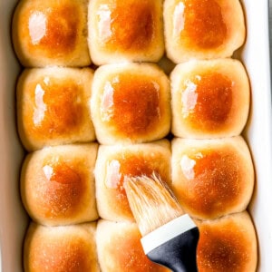 A baking dish filled with buns and a brush.