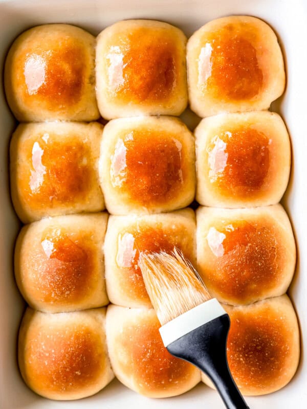 A baking dish filled with buns and a brush.