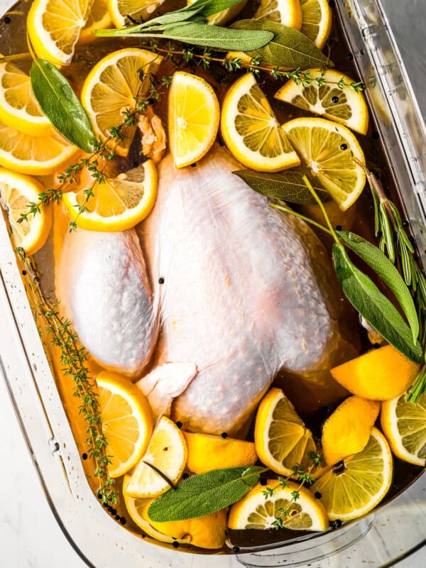 A chicken in a glass dish with lemons and thyme.