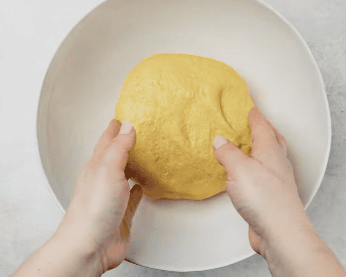 A person placing a smooth, round ball of dough into a white mixing bowl for proofing.