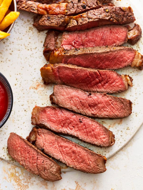 Steak with ketchup and fries on a white plate.