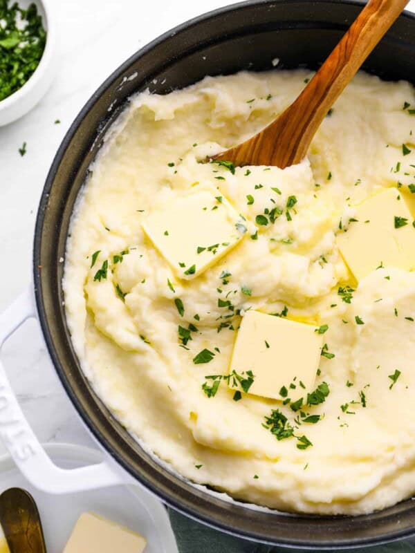 creamy mashed potatoes in a cast iron skillet with a wooden spoon.