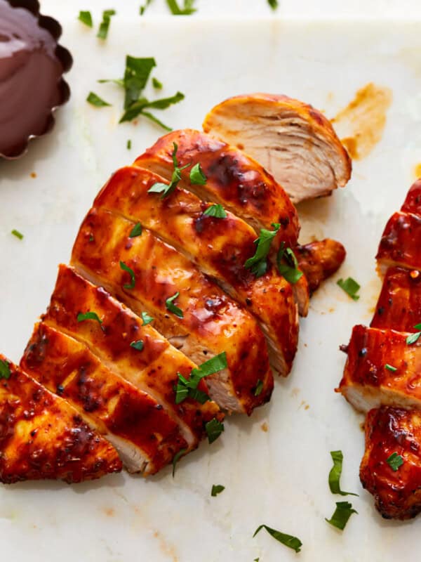 Two air fryer chicken breasts on a cutting board with BBQ sauce and herbs.