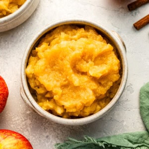 A bowl of applesauce with cinnamon sticks and apples.