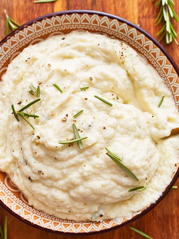 A bowl of mashed cauliflower with rosemary sprigs.