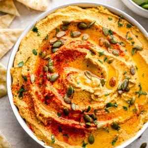 A bowl of hummus with pita chips and seeds.