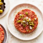 A plate of meat burgers with onions and olives.