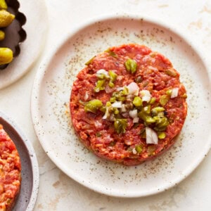 A plate of meat burgers with onions and olives.