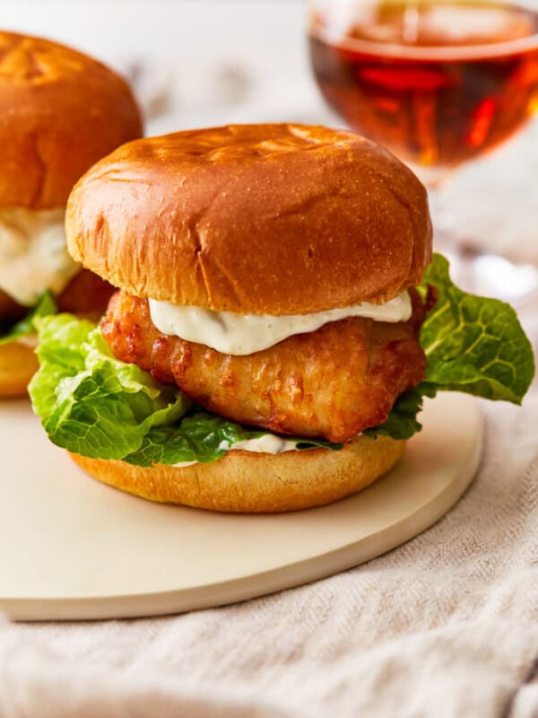 Two fish burgers on a plate next to a glass of beer.