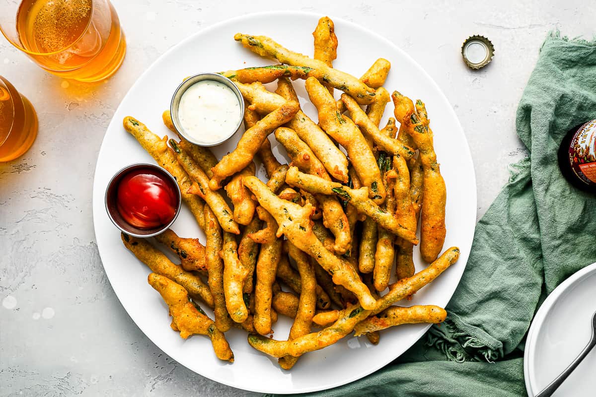 A plate of crispy fried green beans with ketchup and dipping sauce.