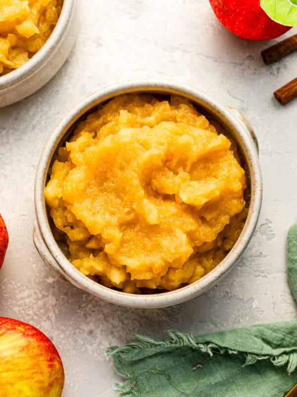 A bowl of applesauce with cinnamon sticks and apples.