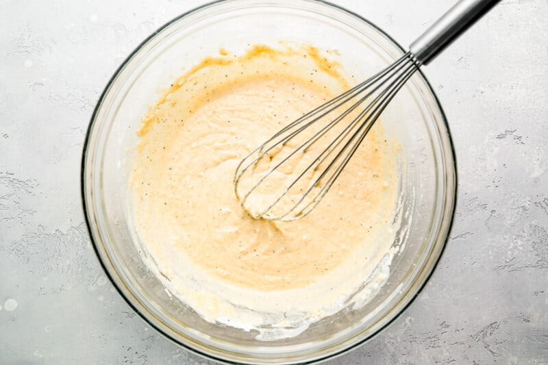 A bowl of batter with a whisk in it.