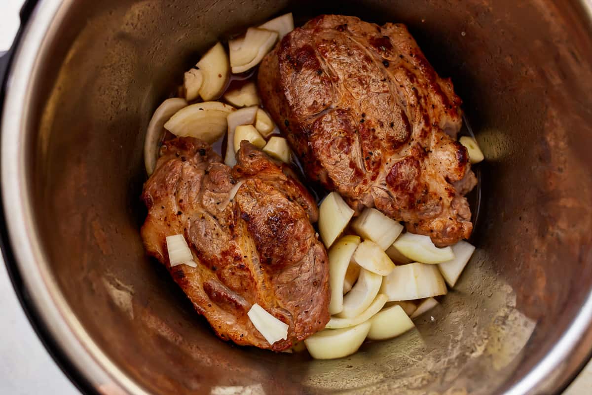 Browned pork shoulder, garlic cloves, and onions in an instant pot.