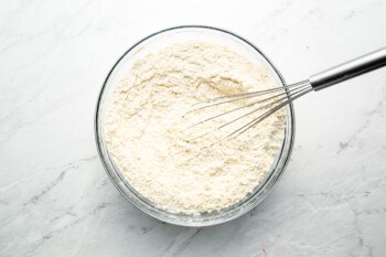 A bowl of flour with a whisk in it.