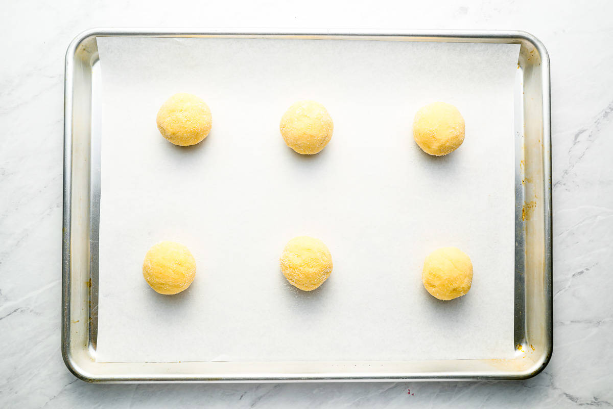 A baking sheet with six cookie dough balls on it.