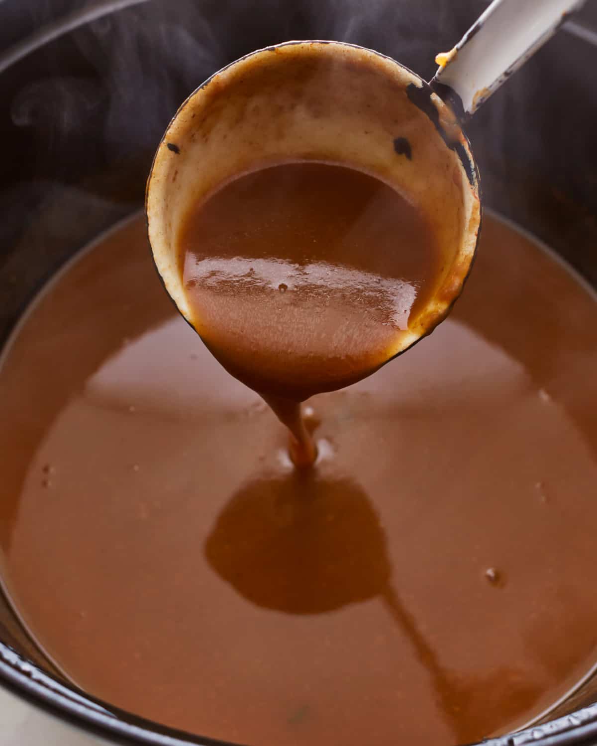 A ladle scooping turkey gravy out of a pot.