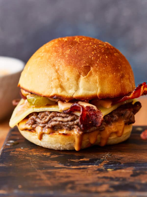 A burger with bacon and cheese on a cutting board.