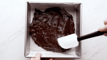 spreading brownie batter in the bottom of a square baking pan with a rubber spatula.