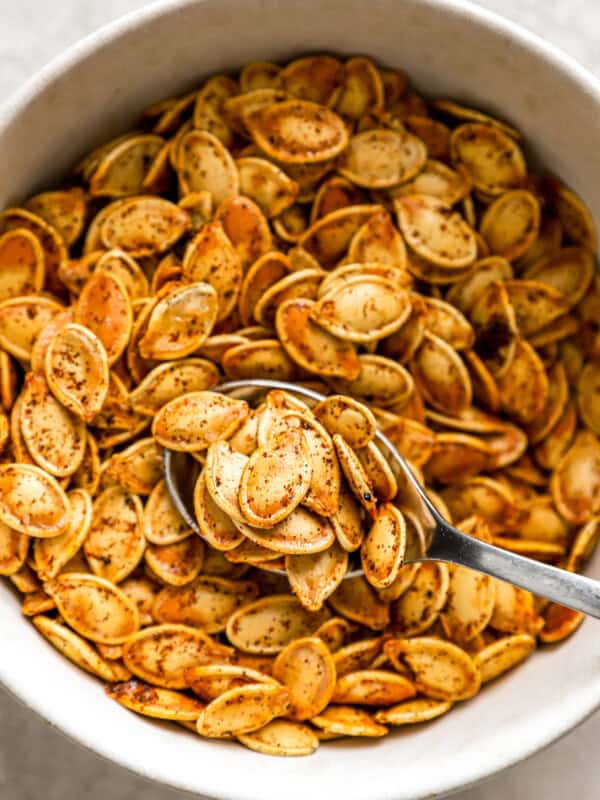 Pumpkin seeds in a white bowl with a spoon.