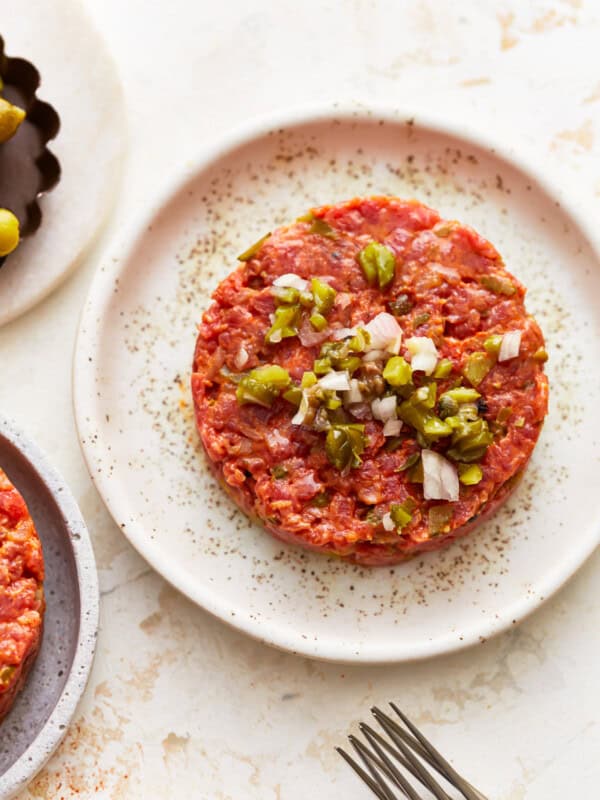 A plate with two meat patties and olives on it.