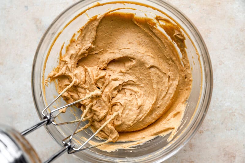 beaten pumpkin and cream cheese in a glass bowl with a hand mixer.