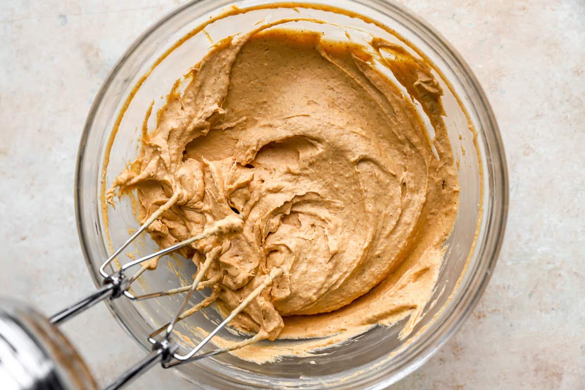 beaten pumpkin and cream cheese in a glass bowl with a hand mixer.