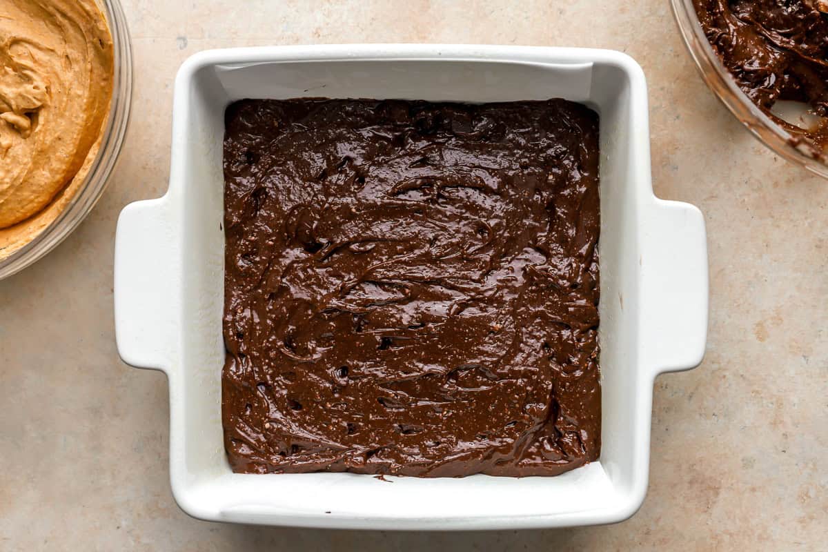 brownie batter poured into the bottom of a square baking pan.