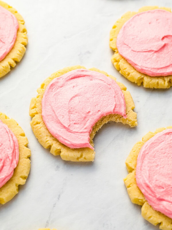 Pink frosted cookies with a bite taken out of them.