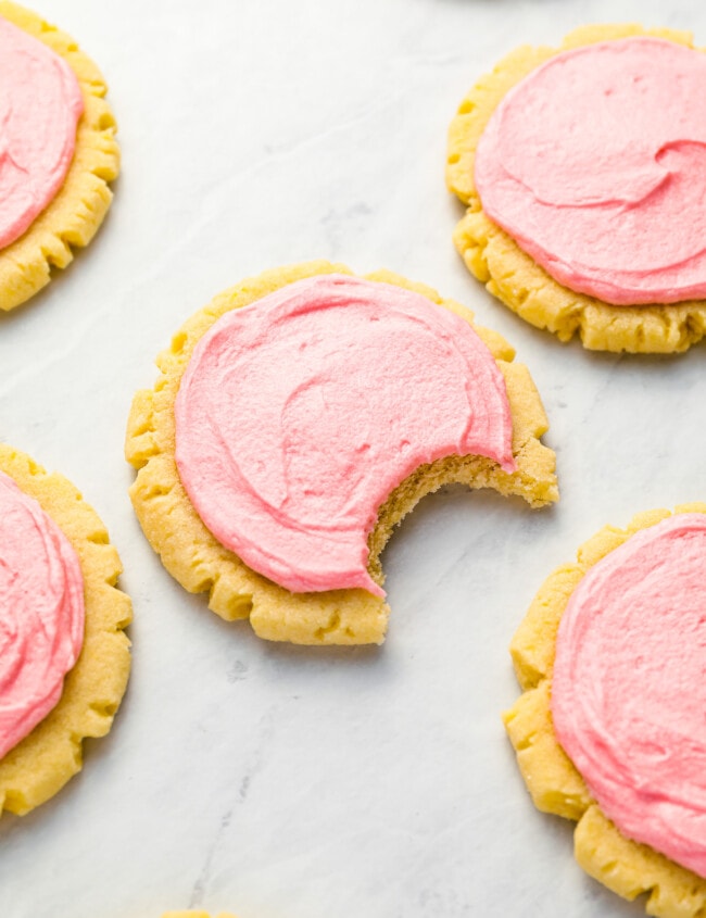Pink frosted cookies with a bite taken out of them.