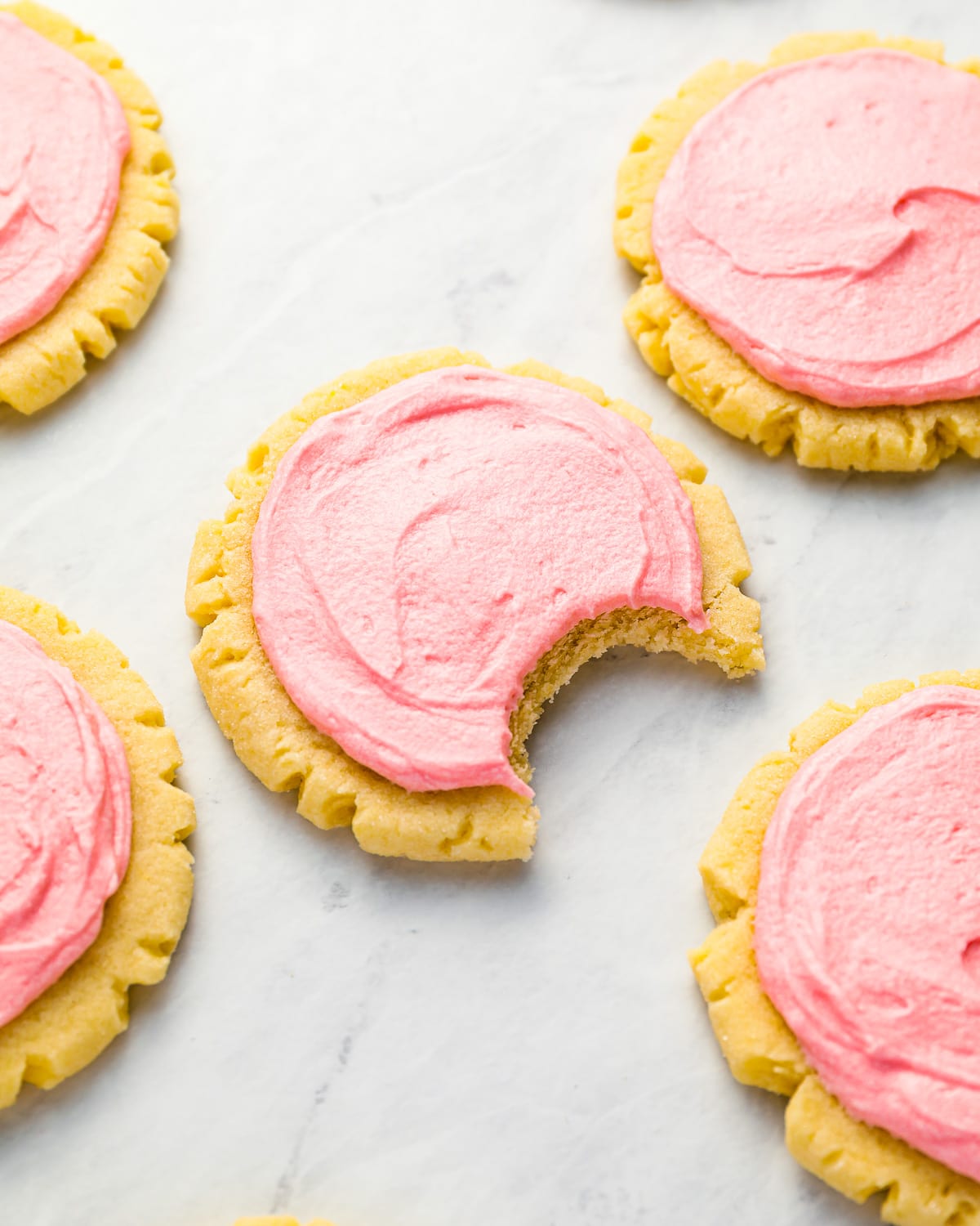 Pink sugar cookies with a bite taken out.