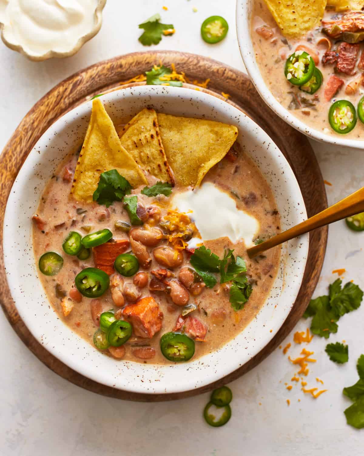 Two bowls of white chicken chili with tortilla chips and sour cream.