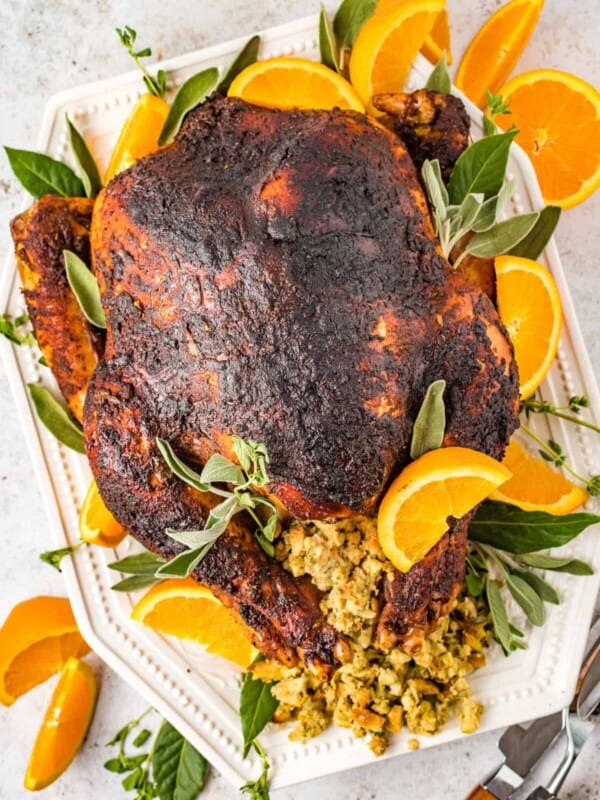 overhead view of dry brined turkey n a white serving dish with sliced oranges and herbs.