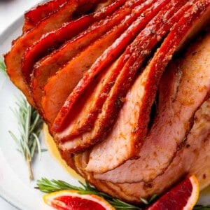 sliced ham with blood oranges and rosemary on a white plate.