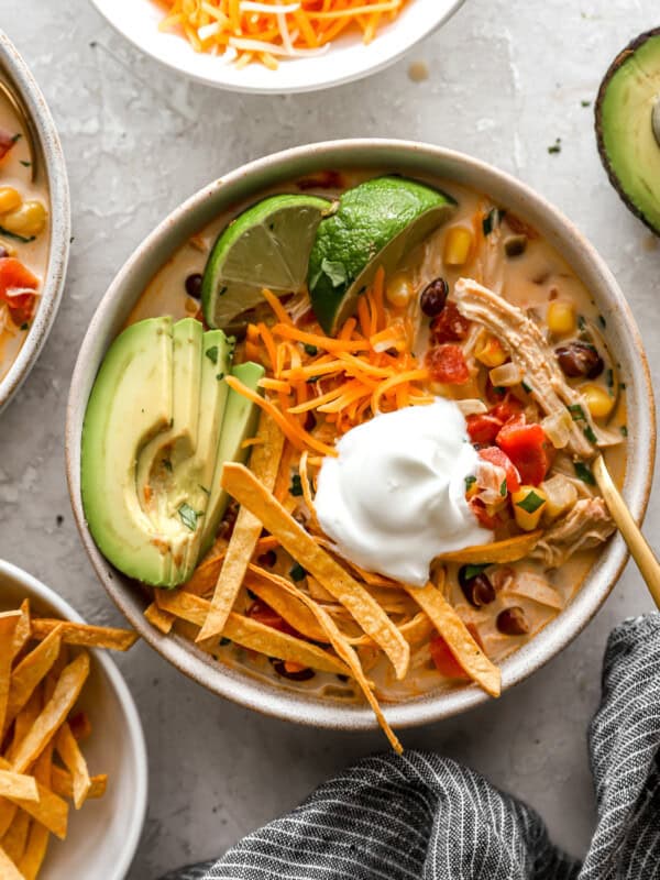 overhead view of a bowl of creamy chicken tortilla soup topped with avocado, tortilla strips, cheese, and sour cream.