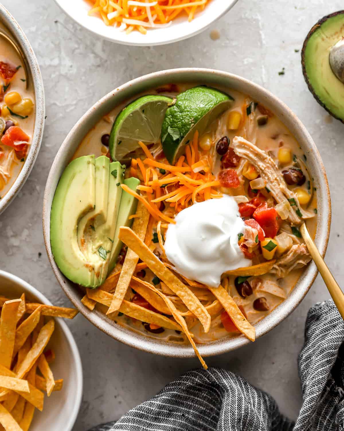 overhead view of a bowl of creamy chicken tortilla soup topped with avocado, tortilla strips, cheese, and sour cream.