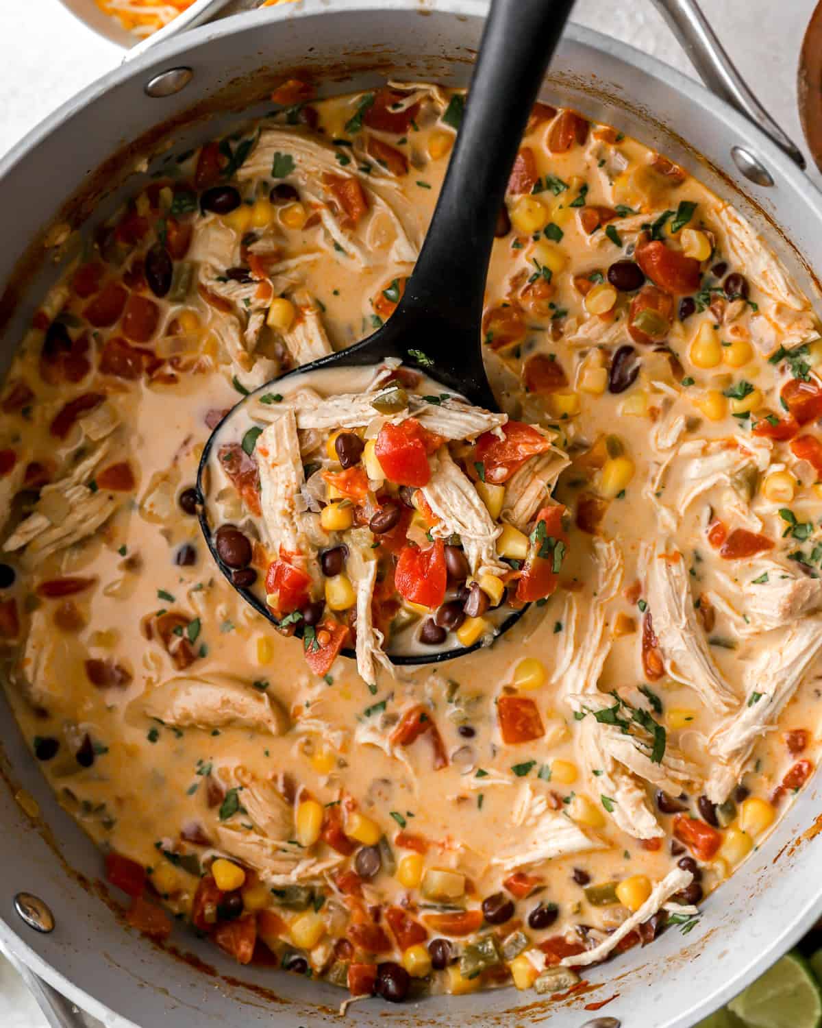 lifting a ladleful of creamy chicken tortilla soup from a dutch oven.