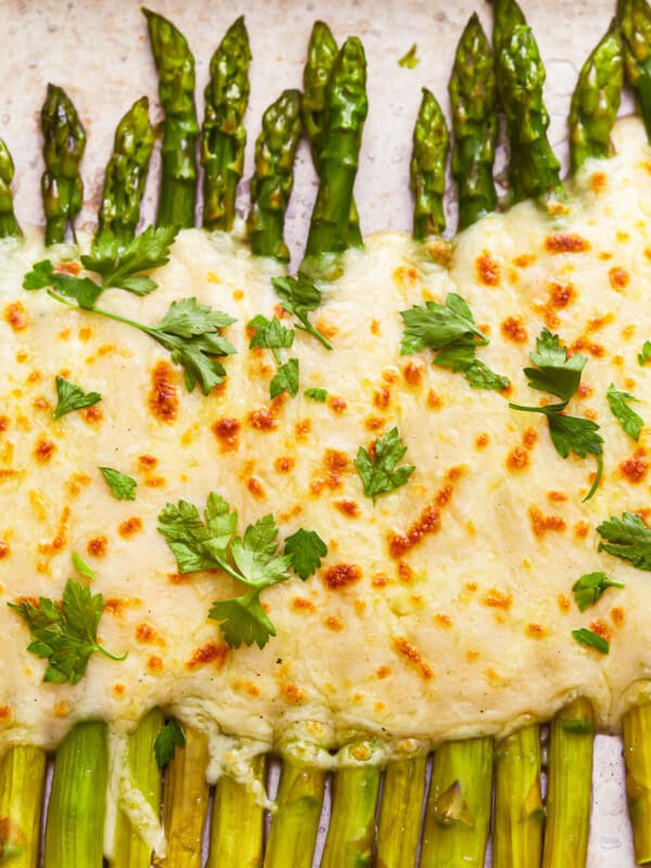 A sheet of asparagus gratin with cheese and parsley on it.