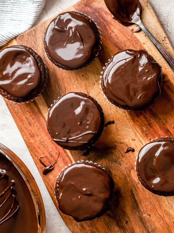 Chocolate cupcakes with chocolate ganache on a wooden cutting board.