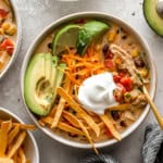 overhead view of a bowl of creamy chicken tortilla soup topped with avocado, tortilla strips, cheese, and sour cream.