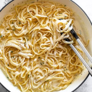 overhead view of fettuccini alfredo in a white dutch oven with tongs.