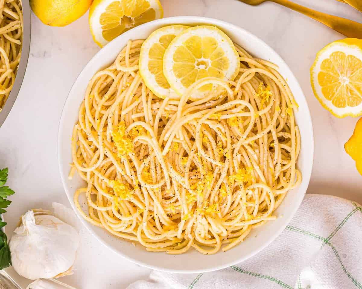 Pasta al limone in a white bowl with lemon slices.