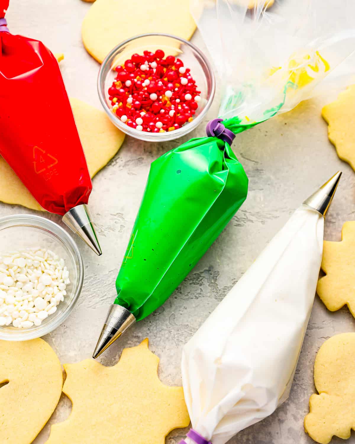 colored royal icing in piping bags with bowls of sprinkles.