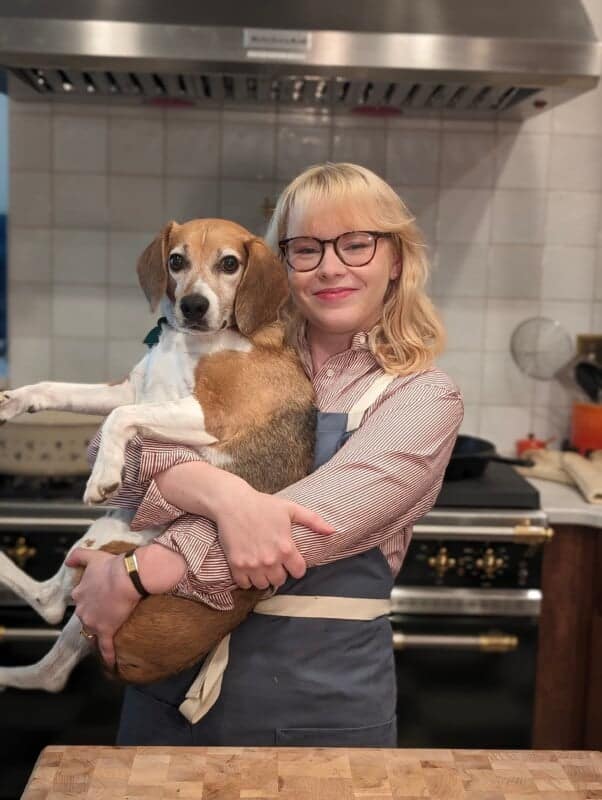 A food blogger holding a dog in a kitchen.