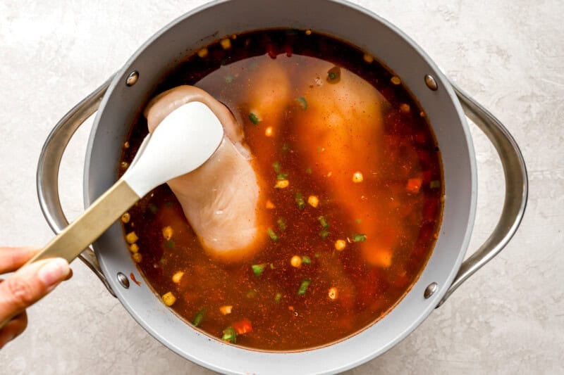 chicken breasts added to tomato broth in a dutch oven with tongs.