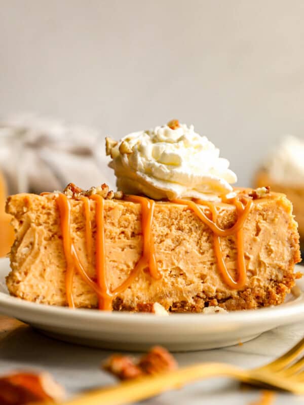 A slice of pumpkin cheesecake on a plate with whipped cream and pecans.