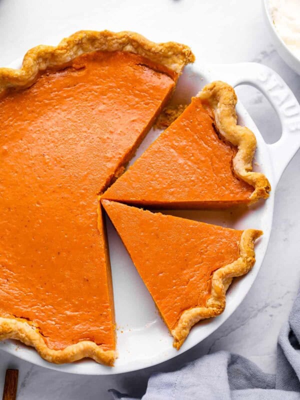 overhead view of a partially sliced sweet potato pie in a white pie pan with handles.