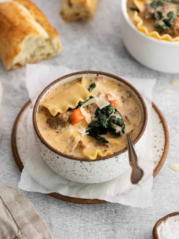 white lasagna soup in a white and brown bowl on a plate with a spoon.