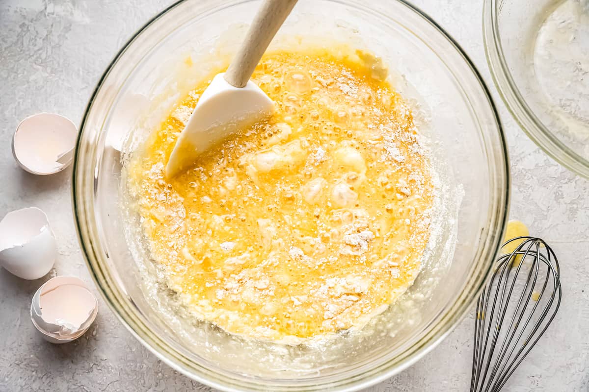 A bowl of batter with eggs and a whisk.