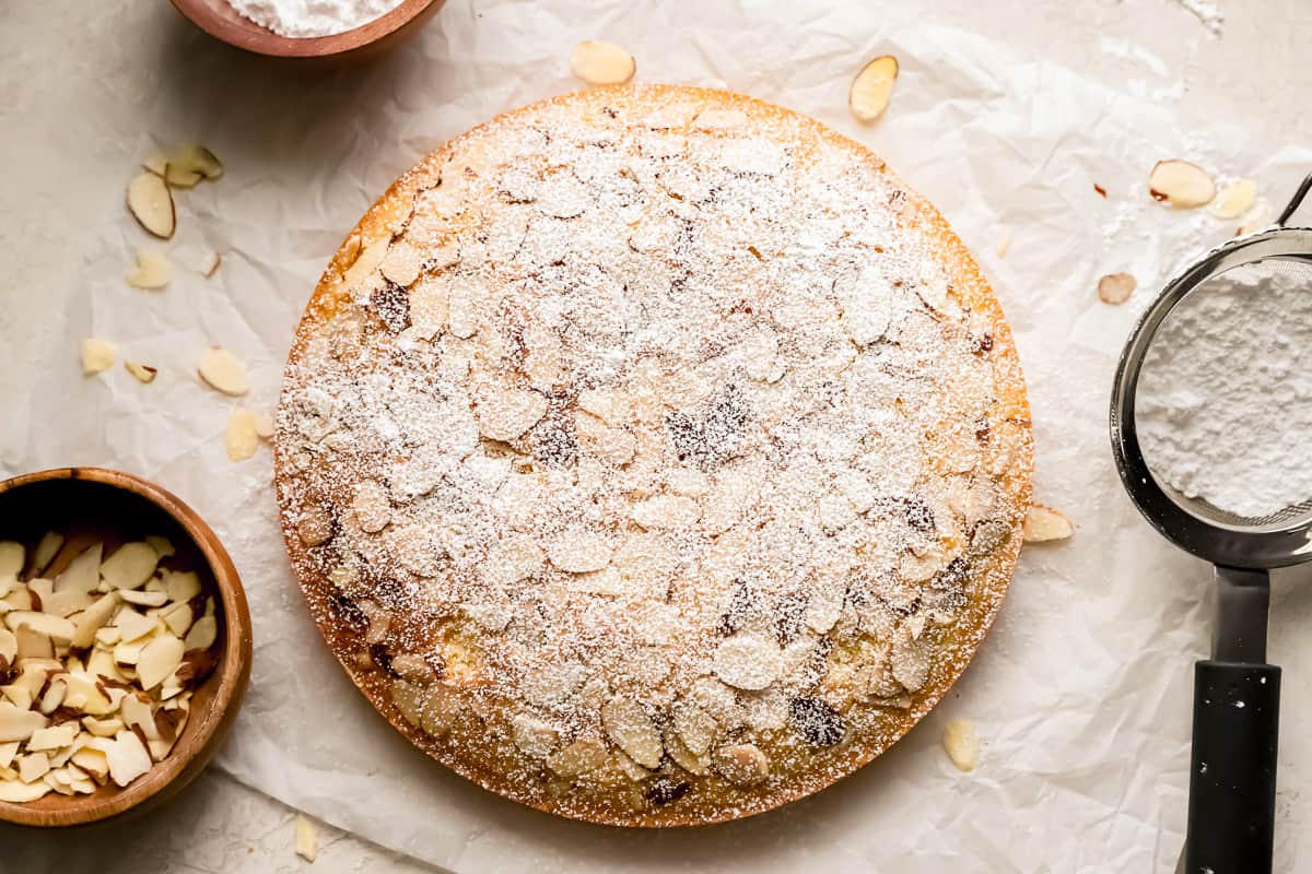 an unsliced almond cake topped with sliced almonds and powdered sugar.